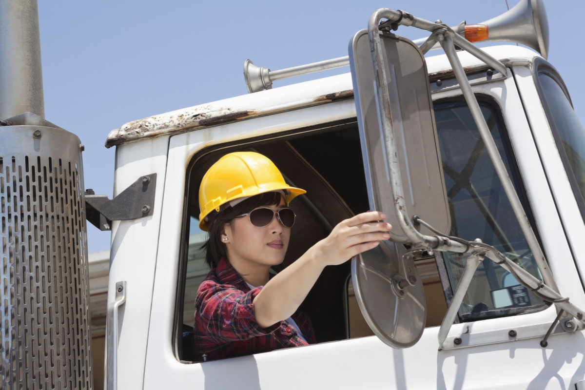 female industrial worker adjusting mirror while sitting in truck